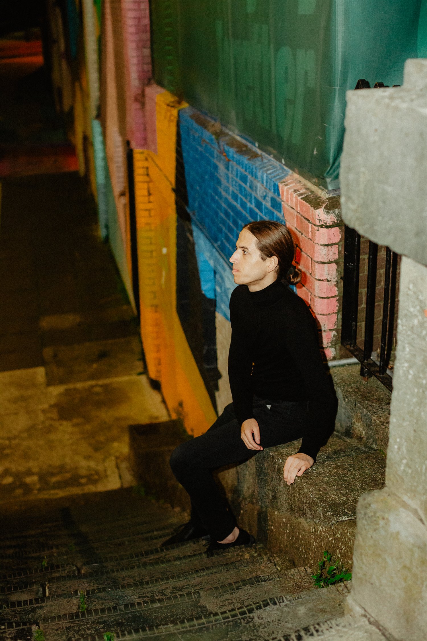 Sebastian Graysen sitting on stone steps at night beside a wall painted in colour